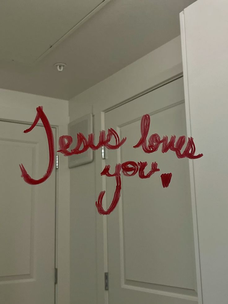 "Red handwritten text on a mirror reads 'Jesus loves you.' The message conveys a positive affirmation of faith and encouragement."